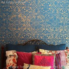 a bed topped with lots of pillows next to a wall covered in blue and gold