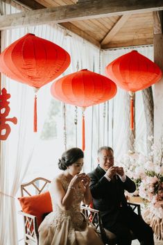 a man and woman sitting next to each other in front of red paper lanterns hanging from the ceiling