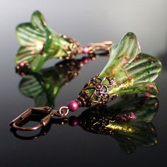 a pair of earrings with green leaves and pink beads on black surface next to mirror