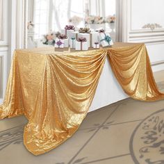 a table covered in gold cloth with presents sitting on top of it next to a window