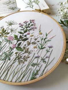 an embroidery project with flowers and leaves on the hoop next to some open book pages