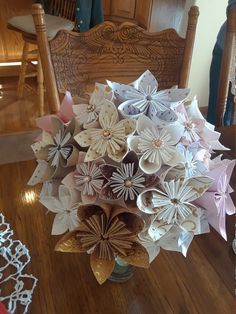 a vase filled with paper flowers sitting on top of a wooden table next to a chair