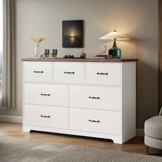 a white dresser with two lamps on top in a living room next to a window