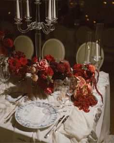 the table is set with red flowers, candles and silverware for an elegant dinner