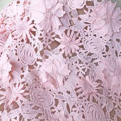 pink crocheted lace with flowers on it is laying on a tablecloth that has been cut in half