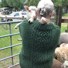 an old woman is holding two lambs on her shoulders while they look at the sheep