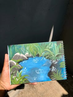 a person holding up a notebook with a painting on it