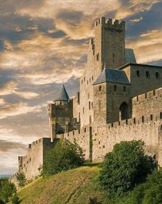 an old castle sitting on top of a lush green hillside under a cloudy blue sky