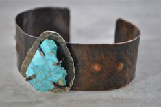 "Handcrafted rustic copper cuff created by hammering, annealing, form folding, drilling, filing, and adding an antique patina. A rough cut turquoise  stone has been attached through the use of prongs The piece has been tumbled for polishing. The inside of this bracelet has been treated with acrylic to prevent tarnish on your skin.  I love making these bracelets and hope you will enjoy wearing one too! INSIDE FIT:  The inner circumference is 6\" with a 1\" gap  This cuff would be considered a medium size. 1 1/4\" wide   3.17 cm  Sizing: Cuffs have approximately a 1\" - 1 1/4\" opening and this can be adjusted either way with slight pressure for your custom fit. This allows you to use the gap in the bracelet for putting on and taking off.  Your cuff will be placed in a gift box with a cotton Rustic Turquoise Bracelet Jewelry, Handmade Turquoise Artisan Cuff Bracelet, Rustic Turquoise Bracelet, Unique Adjustable Jewelry With Patina, Artisan Jewelry With Patina And Adjustable Fit, Adjustable Hammered Turquoise Jewelry, Earthy Hand Forged Adjustable Jewelry, Adjustable Artisan Hammered Jewelry, Artisan Hammered Turquoise Jewelry