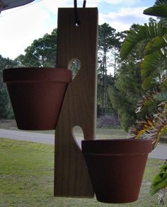 two brown pots are hanging from a wooden rack in the grass near a tree and road