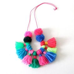 two colorful tassels hanging from a string on a white surface with pink, green, and blue yarn