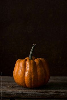 a small orange pumpkin sitting on top of a wooden table next to a brown wall