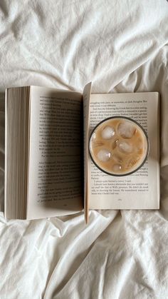 an open book sitting on top of a bed next to a cup of coffee and ice