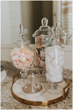 three glass jars filled with candy on top of a marble counter next to a mirror