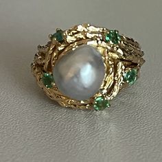 Ring in chiseled yellow gold wire (18k) adorned with a baroque gray Akoya pearl surrounded by 5 emeralds. French work around 1950-60. Pearl diameter: 9 to 9.6 mm. Gross Weight: 9.50 g. Size: 49 Possibility of sizing, contact us. Further information : We issue an invoice as well as a certificate of authenticity established by our qualified gemologist (LFG Paris). Our photos are not reworked and are taken in a natural light environment. We can send you a short video upon simple request. Each piece Emerald Style, Vintage Jewellery Rings, Akoya Pearls, Vintage Jewels, Gold Wire, Multi Stone Ring, Multi Stone, Emerald Ring, Green Stone