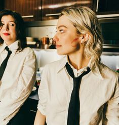 two women in white shirts and black ties sitting next to each other on a counter