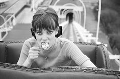 black and white photograph of a woman eating food in an amusement park ride area with roller coasters behind her