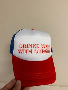 Head out in style with the Drinks Well With Others trucker hat! This one-of-a-kind, tri-colored design looks and feels awesome, so you can make a statement without saying a word. Plus, the adjustable snapback ensures everyone can enjoy this fashionable accessory. Get ready to turn heads! Funny Snapback Baseball Cap, Funny Trucker Hat For Streetwear, Funny Trucker Hat With Curved Brim, Novelty Red Trucker Hat, Funny Snapback Hat With Letter Print, Fun Red Snapback Trucker Hat, Funny White Trucker Hat Baseball Cap, Funny White Baseball Cap Trucker Hat, Funny Trucker Hat With Letter Print