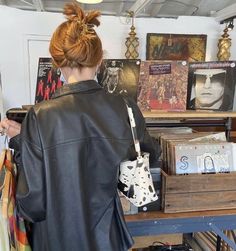 a woman in a black leather jacket looking at records on a shelf and holding a purse