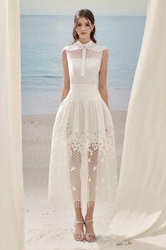 a woman is standing on the beach wearing a white dress