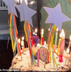 a birthday cake with lit candles and stars on it, in front of a man's face