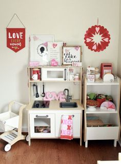 a toy kitchen set up in a child's playroom with wooden floors and white walls