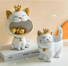 two white cats with gold crowns on their heads and one is holding a bowl full of chocolates