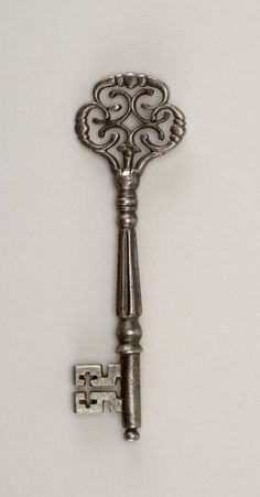 an antique silver key with filigrees on the front and back ends is displayed against a white background