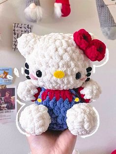 a hand holding a hello kitty crochet doll in front of a white wall