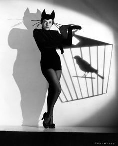 black and white photograph of a woman in cat costume holding a birdcage with one hand