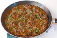 a pan filled with meat and vegetables on top of a table next to a blue towel