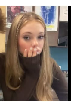 a woman with long blonde hair sitting in front of a computer desk while holding her hand up to her mouth