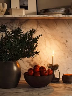 an arrangement of apples in a bowl on a table with a lit candle and plates