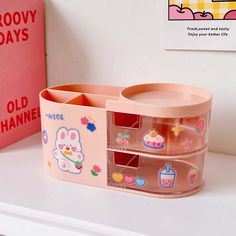 a pink plastic storage container sitting on top of a white counter next to a red book