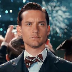 a man in a suit and bow tie looking at the camera with fireworks in the background