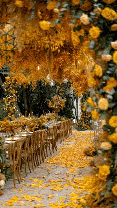 a long table covered in yellow flowers and greenery with lots of chairs around it