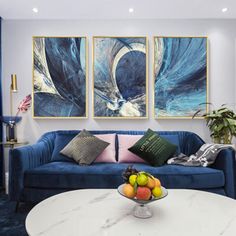 a living room with blue couches and paintings on the wall above them, along with a bowl of fruit