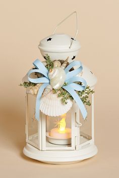 a small white lantern with a blue ribbon around it and a lit candle in the middle