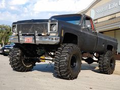 a large black truck parked in front of a store with big tires on it's tires