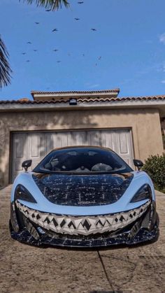 a blue sports car parked in front of a house next to a palm tree and birds