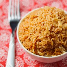 a white bowl filled with rice next to a fork and knife on a red table cloth