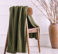 a chair with a green blanket on it next to a vase filled with dried branches