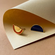 two gold and blue earrings sitting on top of a piece of paper next to each other