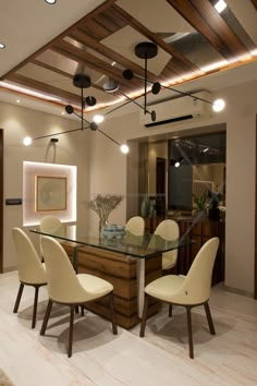 a dining room table with white chairs and lights on the ceiling above it is an open kitchen area