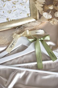 two hangers with ribbons tied to them sitting on a satin surface next to a painting