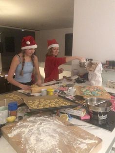 two girls in santa hats making cookies on a kitchen counter top with other baking supplies