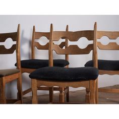 three wooden chairs with black cushions against a white wall