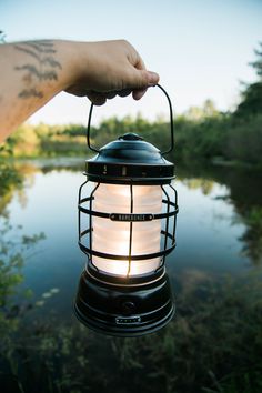 a person is holding a lantern in front of the water with their hand on it