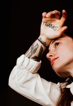 a woman with tattoos on her arm and hand holding up the word thanks above her head