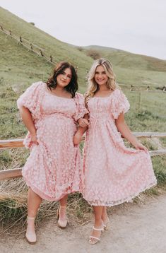 two women standing next to each other on a dirt road in front of a fence